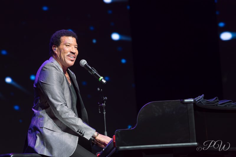 A singer at a piano smiling into the microphone on stage
