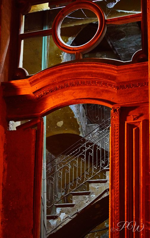 A red wooden doorway with a round window opens onto a spiral staircase