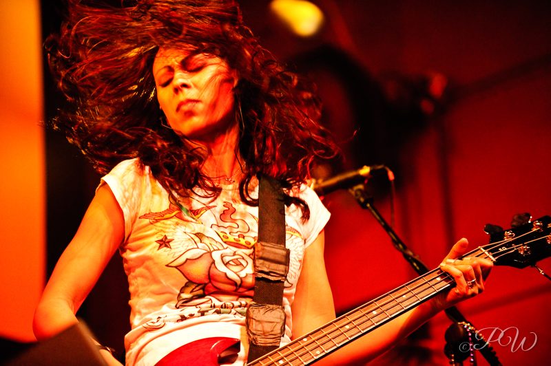 A bass player with flying hair performing under red light with Cowboy Mouth