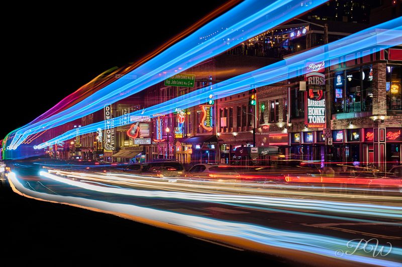 Light trails streak past the neon signs of Broadway at night