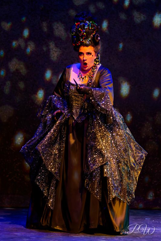 An actress in an elaborate brocade gown and feathered headdress on stage