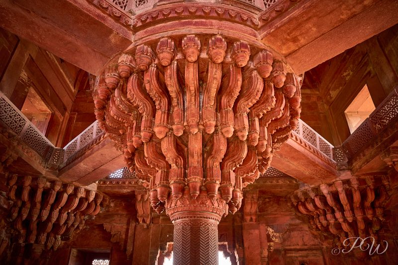 An elaborately carved red sandstone pillar and its radiating brackets inside a hall