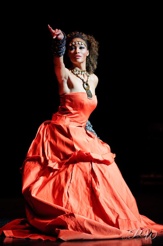 A model in a voluminous red gown posing on a dark runway