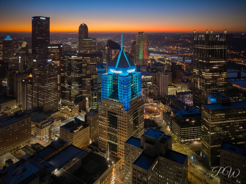 Aerial view of downtown Pittsburgh at dusk with a blue-lit tower in the centre