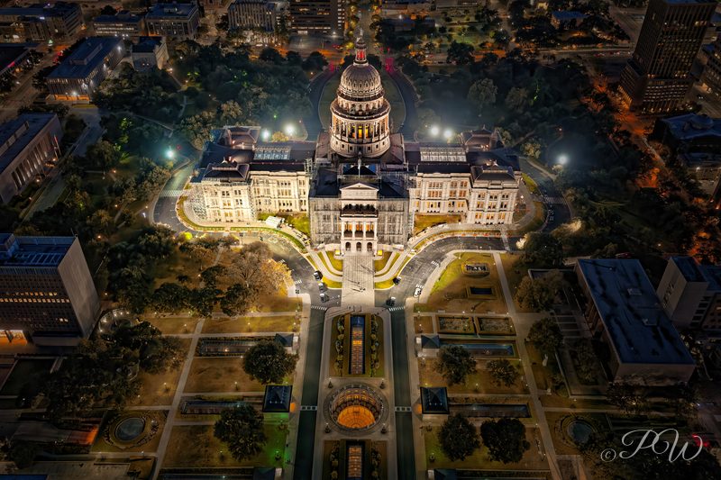 Aerial view of the lit Texas State Capitol and its grounds at night