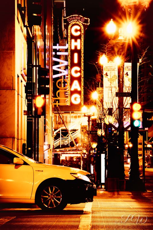 The lit CHICAGO marquee sign above a yellow taxi at night