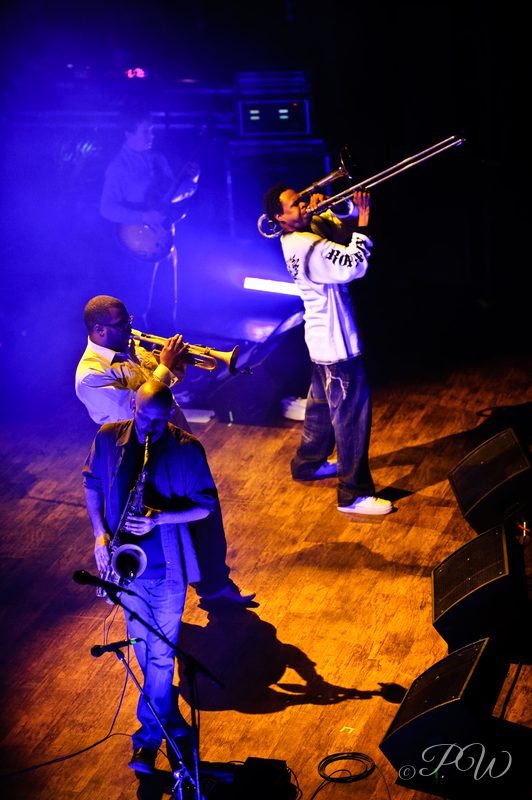 Horn players from Galactic performing under blue and orange stage light