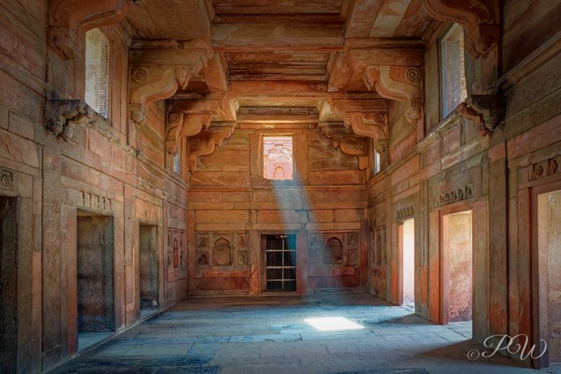 A shaft of sunlight falls across the floor of a painted stone hall