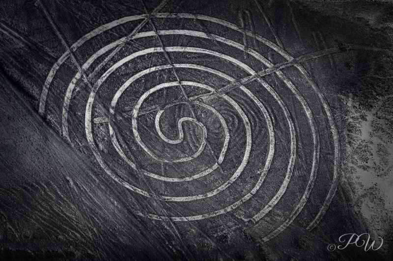 A large spiral etched into the desert floor, seen from the air in black and white