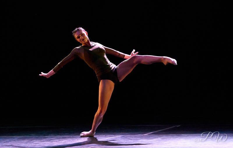 A dancer holds an arabesque on a dark stage