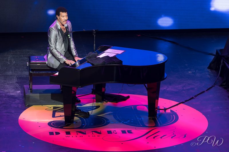 A performer at a grand piano on a stage with a pink light circle