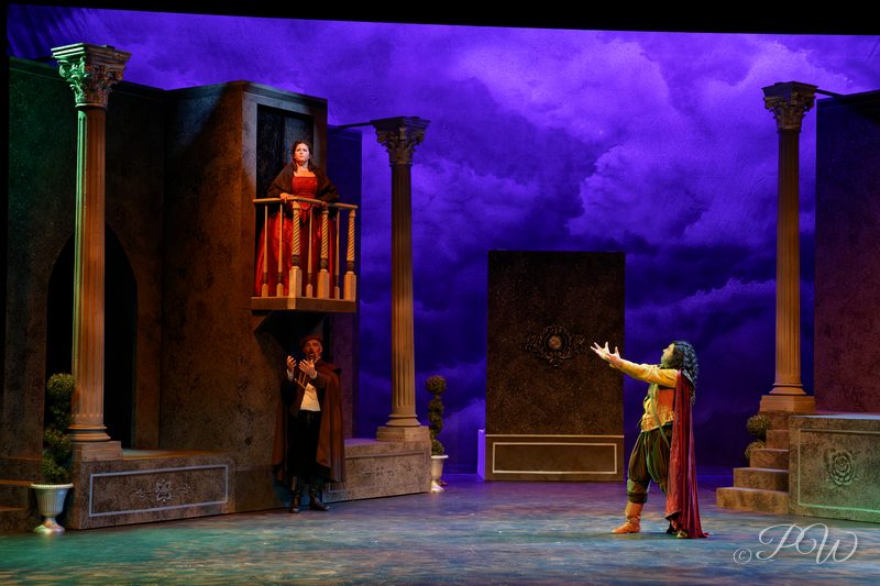Actors on a classical stage set with stone columns under a painted purple sky