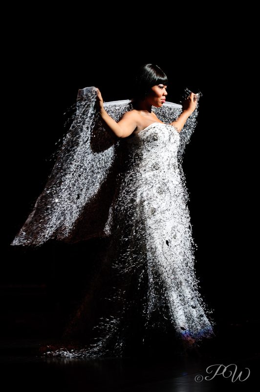 A model in a silver sequined gown with a dramatic collar on a dark runway