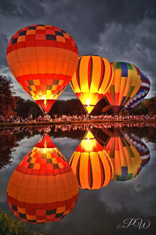 Glowing hot air balloons reflected in a pond at twilight
