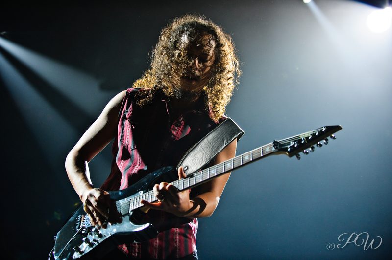 A curly-haired Metallica guitarist playing under white stage light