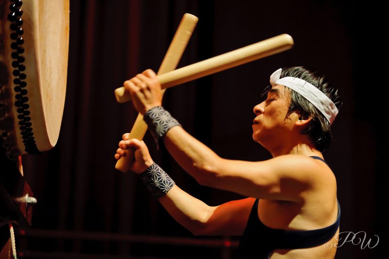 A taiko drummer with raised sticks against a dark background