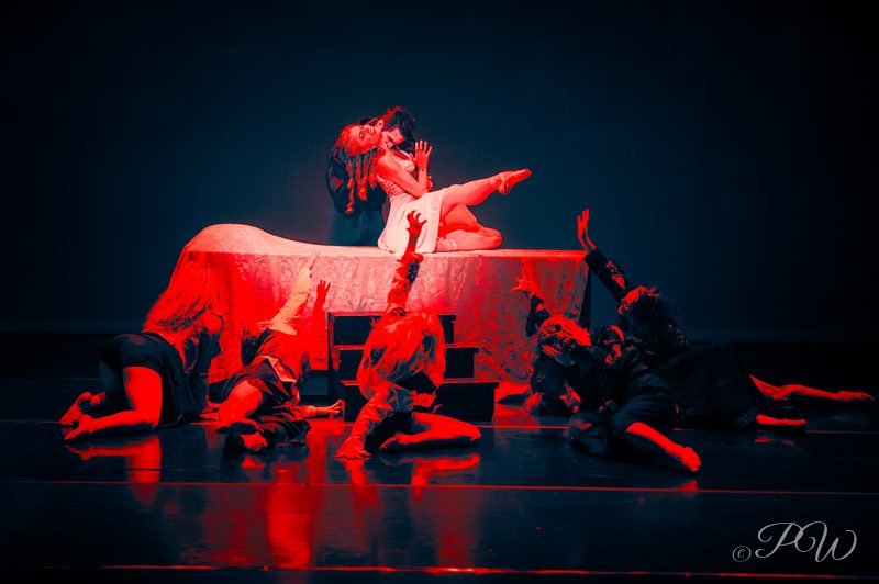 A dance ensemble on the floor of a stage lit in red