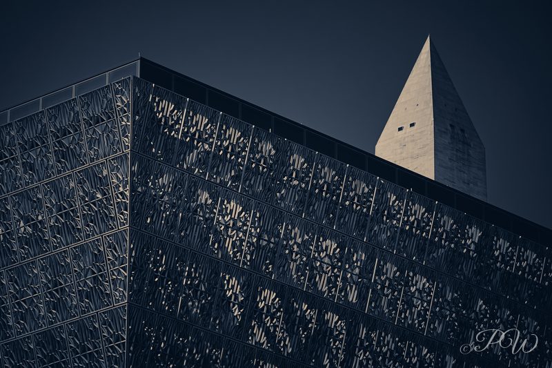 A dark bronze lattice facade in the foreground with the Washington Monument behind