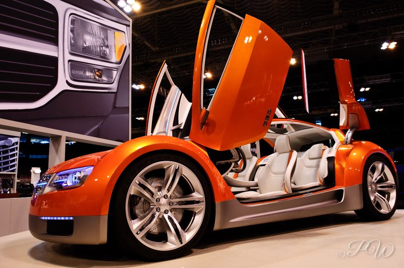 An orange concept car with scissor doors raised, on display at an auto show