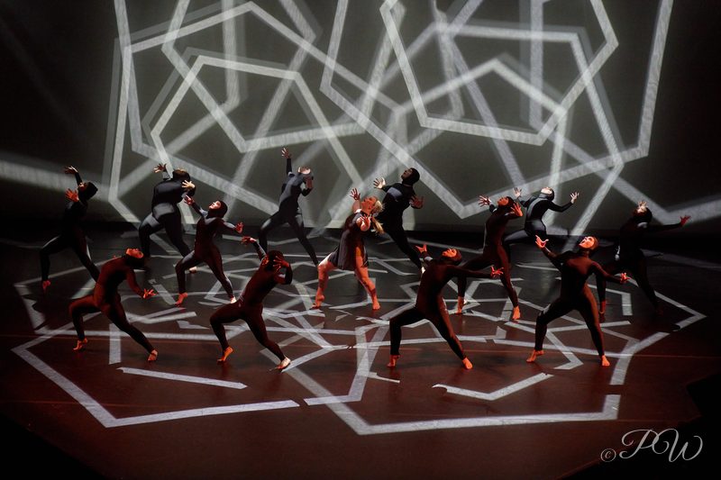 A group of dancers under a projected white geometric light pattern