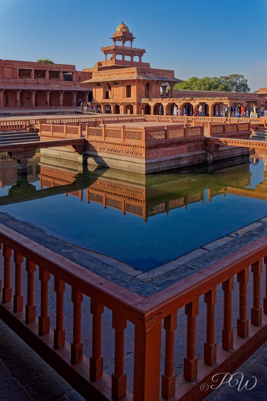 A red sandstone pavilion and balustrade reflected in a still pool