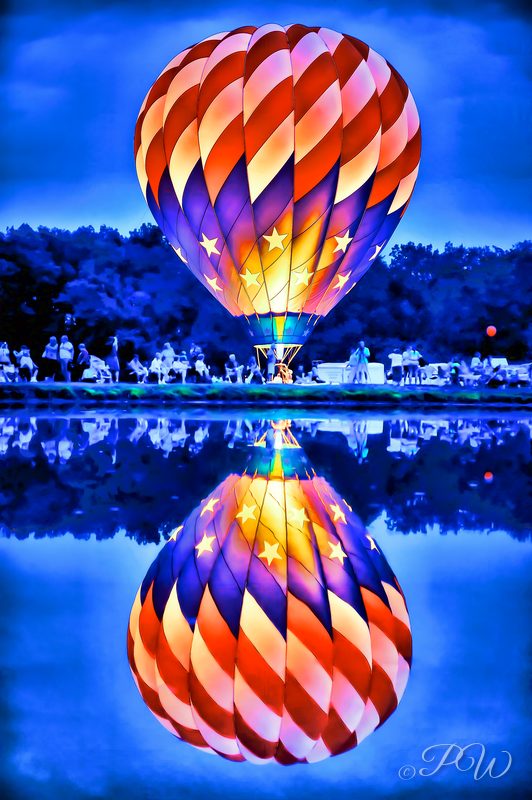 A single glowing hot air balloon mirrored in still water at twilight